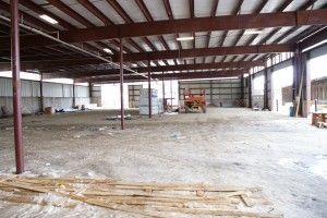 Empty warehouse interior with steel beams, concrete floor, and scattered debris