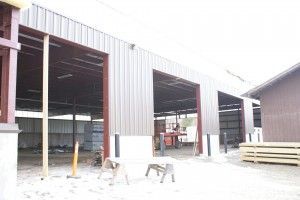 Large metal warehouse under construction with open bays and scattered materials outside