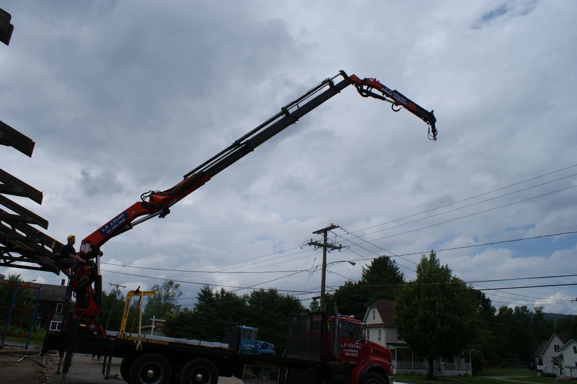 Red crane truck extends a long boom over houses under a cloudy sky.