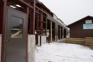 Snowy outdoor walkway beside a building with large windows and stacked wooden boards