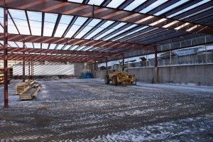 Empty industrial warehouse interior with steel beams, concrete floor, and a yellow forklift near stacked materials