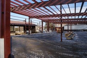 Partially built steel-framed structure with red beams and gravel floor under construction