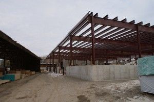 Construction site with steel building frame and concrete walls beside a dirt road