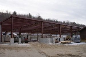 Steel-framed building under construction on a muddy site, with concrete columns and open sides
