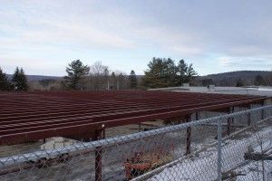 Row of red farm equipment behind a chain-link fence in a snowy rural field