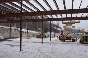 Snowy construction site with steel beams, a crane lift, and workers near equipment