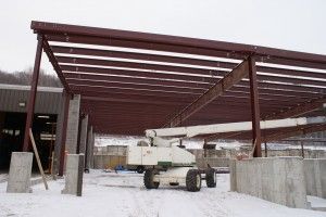 Snow-covered construction site with a white lift under a red steel canopy frame