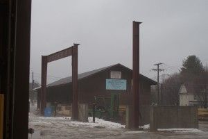 Snowy industrial yard with tall rust-red steel frames and a dark-roofed building in foggy weather