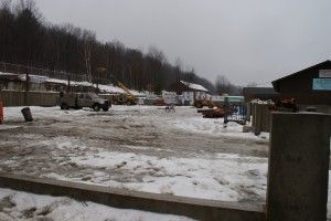 Snowy industrial yard with parked trucks and buildings under an overcast sky