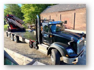 Black tow truck with red boom parked beside a brick building on a gravel lot