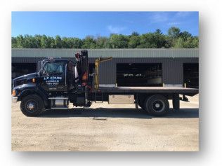 Black flatbed tow truck parked in front of a building on a sunny day.