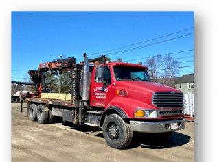Red semi-truck hauling construction equipment on a flatbed trailer outdoors on a sunny day