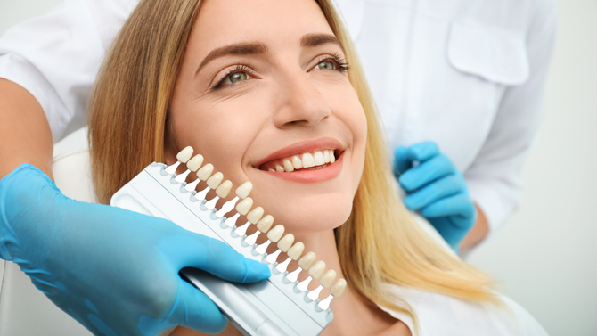 Dentist holding shade guide near smiling patient in a dental clinic