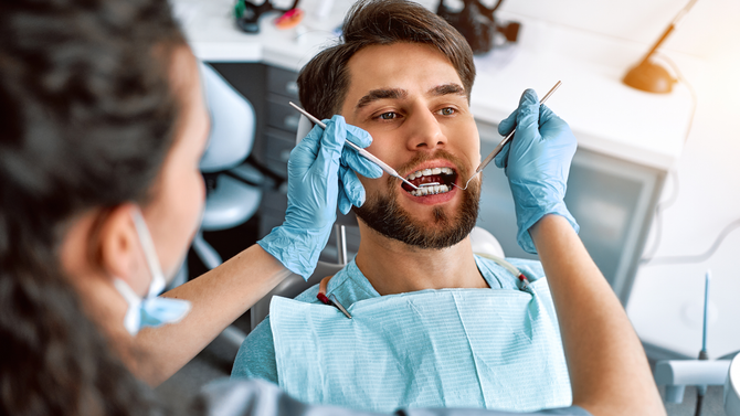 Dentist examining a patient’s open mouth with dental tools in a bright clinic