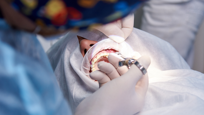 Dentist examining a patient’s open mouth with dental tools in a bright clinic