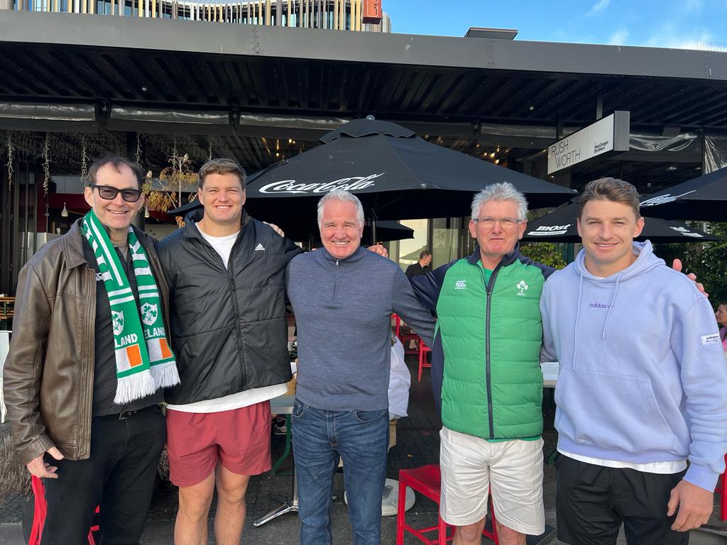 Five people posing together outdoors; some wearing Irish green.