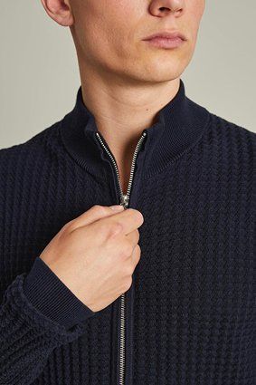 Person zipping up a navy blue textured cardigan.