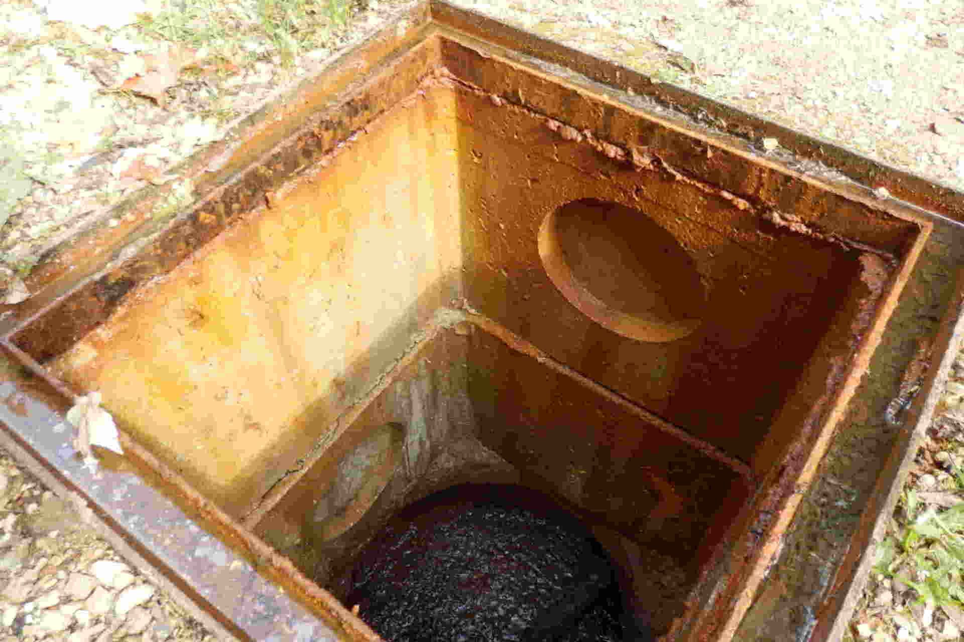 Open rusty metal manhole leading to a dark underground chamber with a round pipe opening