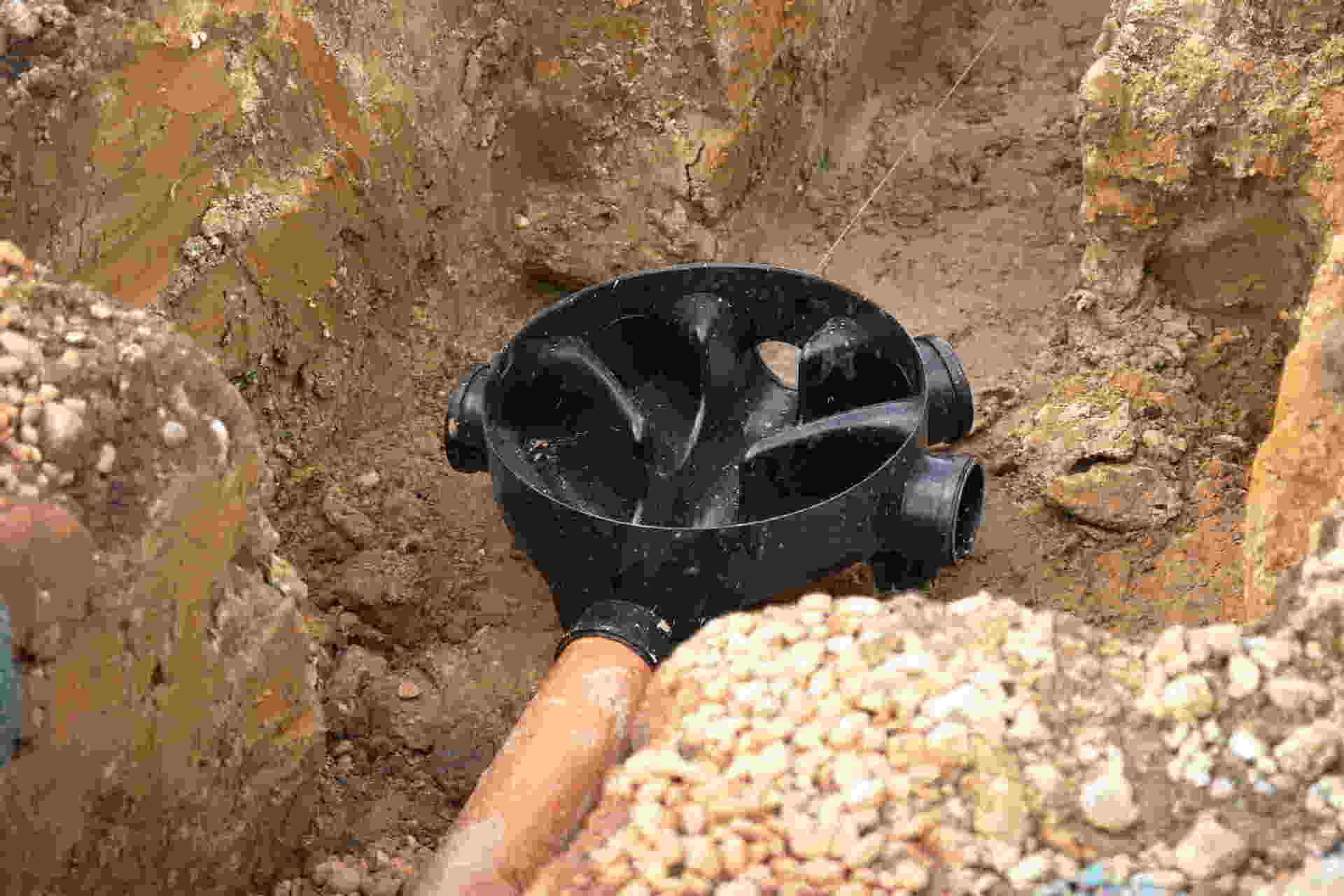 Black metal detector coil probing a muddy trench with gravel and bricks around it