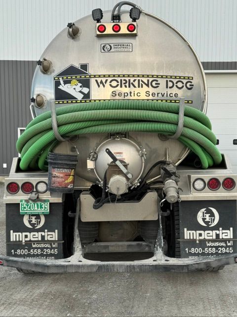 Sewer truck with a large white tank and red hose pumping liquid on a sunny street