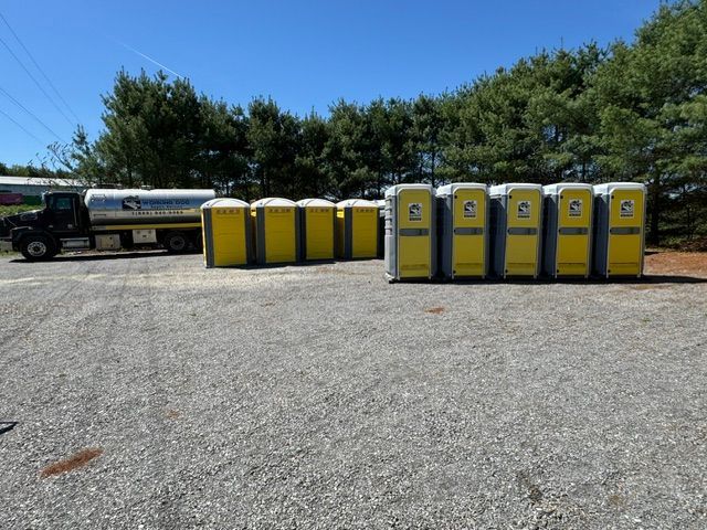 Row of portable toilets beside a grassy path in a park-like outdoor setting