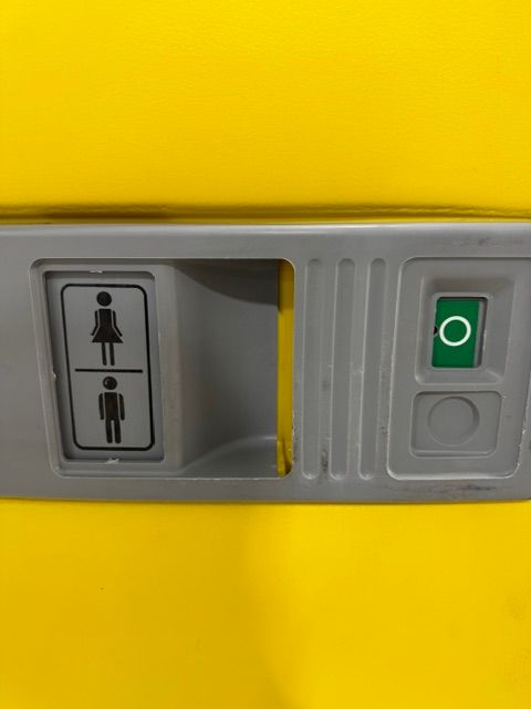 Bathroom gender sign with female and male icons on a gray panel, next to a yellow-green indicator bar