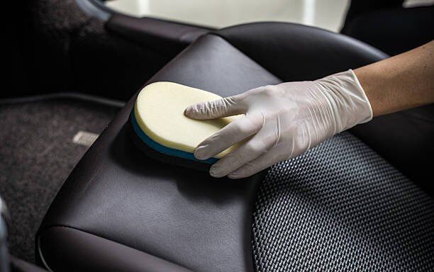Una persona con guantes está limpiando el asiento de un automóvil con una esponja.