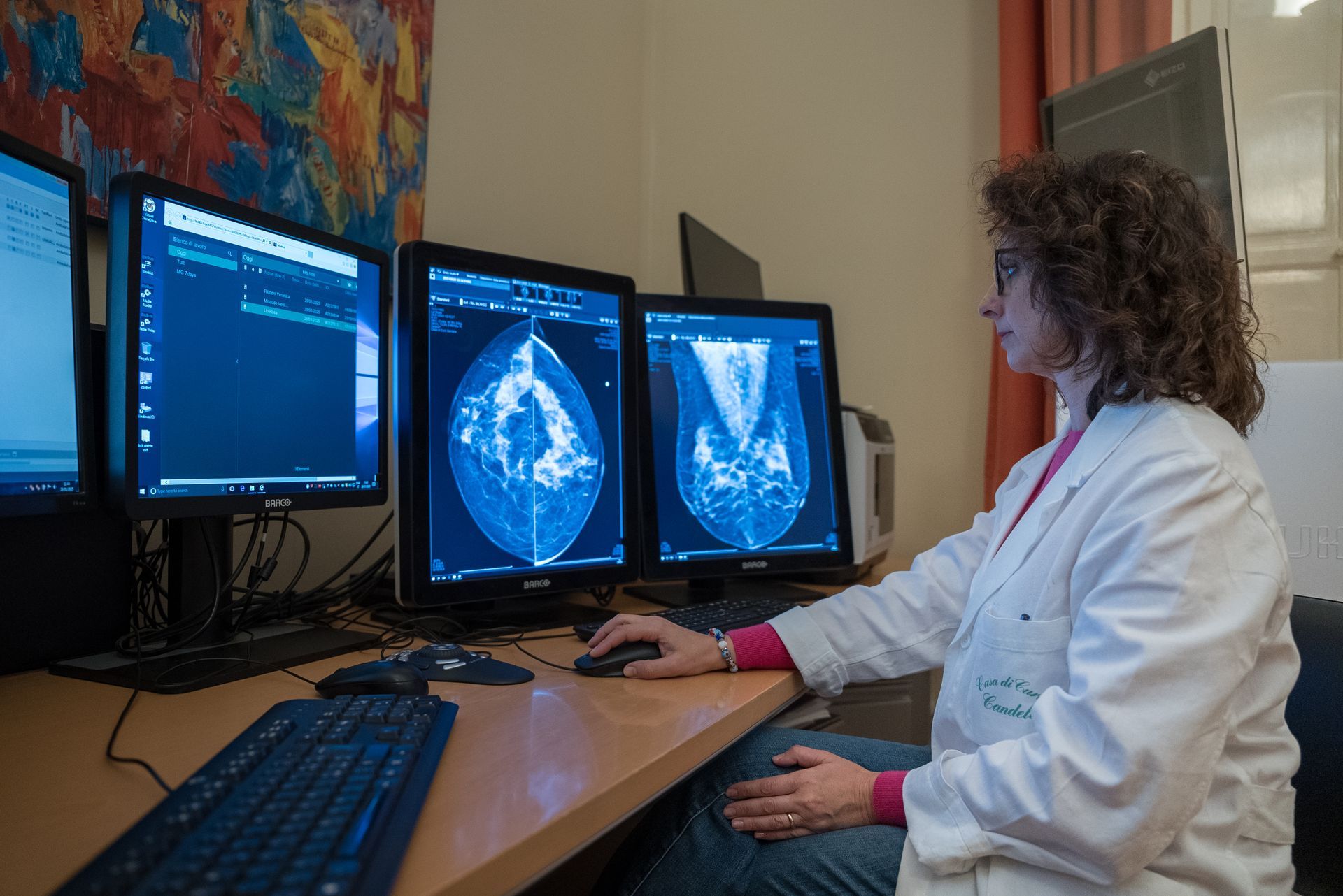 Una donna in camice è seduta a una scrivania davanti a tre monitor di computer.