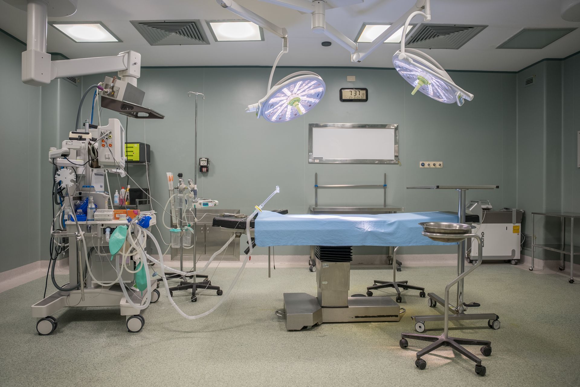 Una sala operatoria vuota con un tavolo blu e un sacco di attrezzature mediche