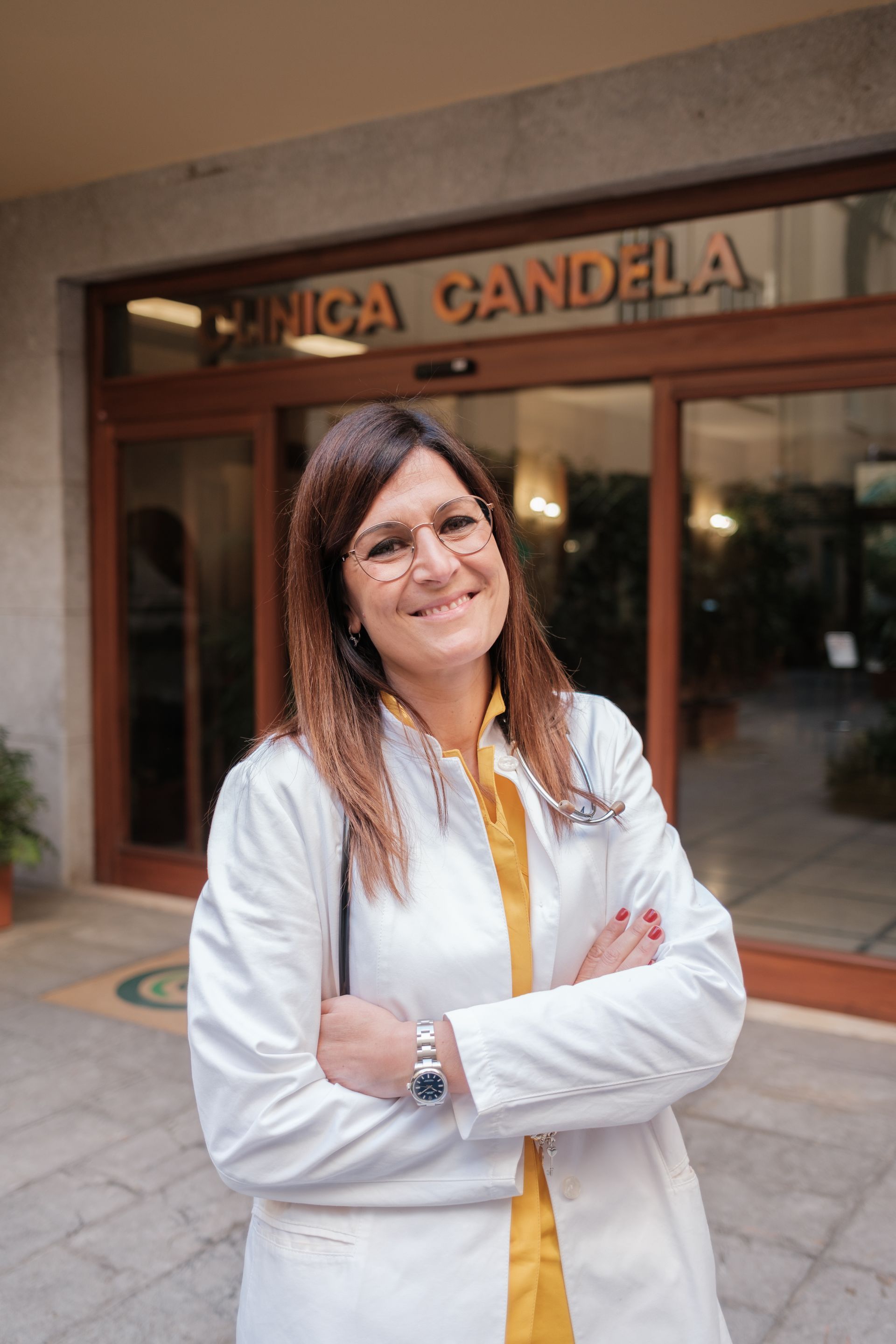 Una donna in camice bianco è in piedi davanti a un edificio con le braccia incrociate.