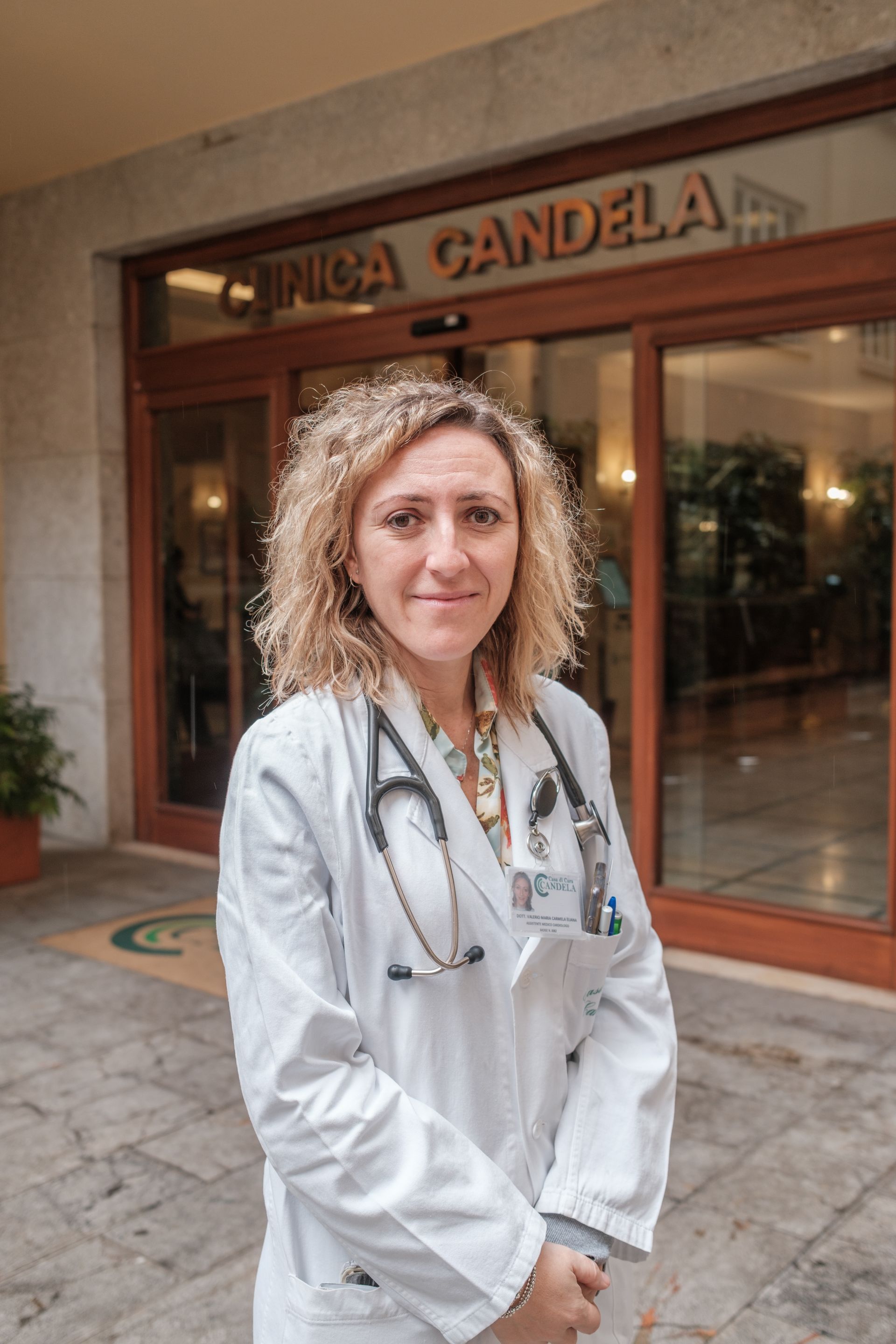 Una donna in camice e con uno stetoscopio al collo è in piedi davanti a un edificio.
