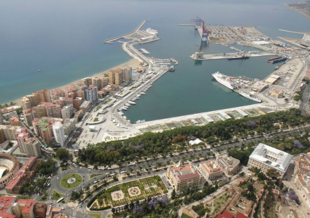 Puerto de Málaga visto desde el aire, con muelles, barcos y áreas verdes, integrado en el entorno urbano.