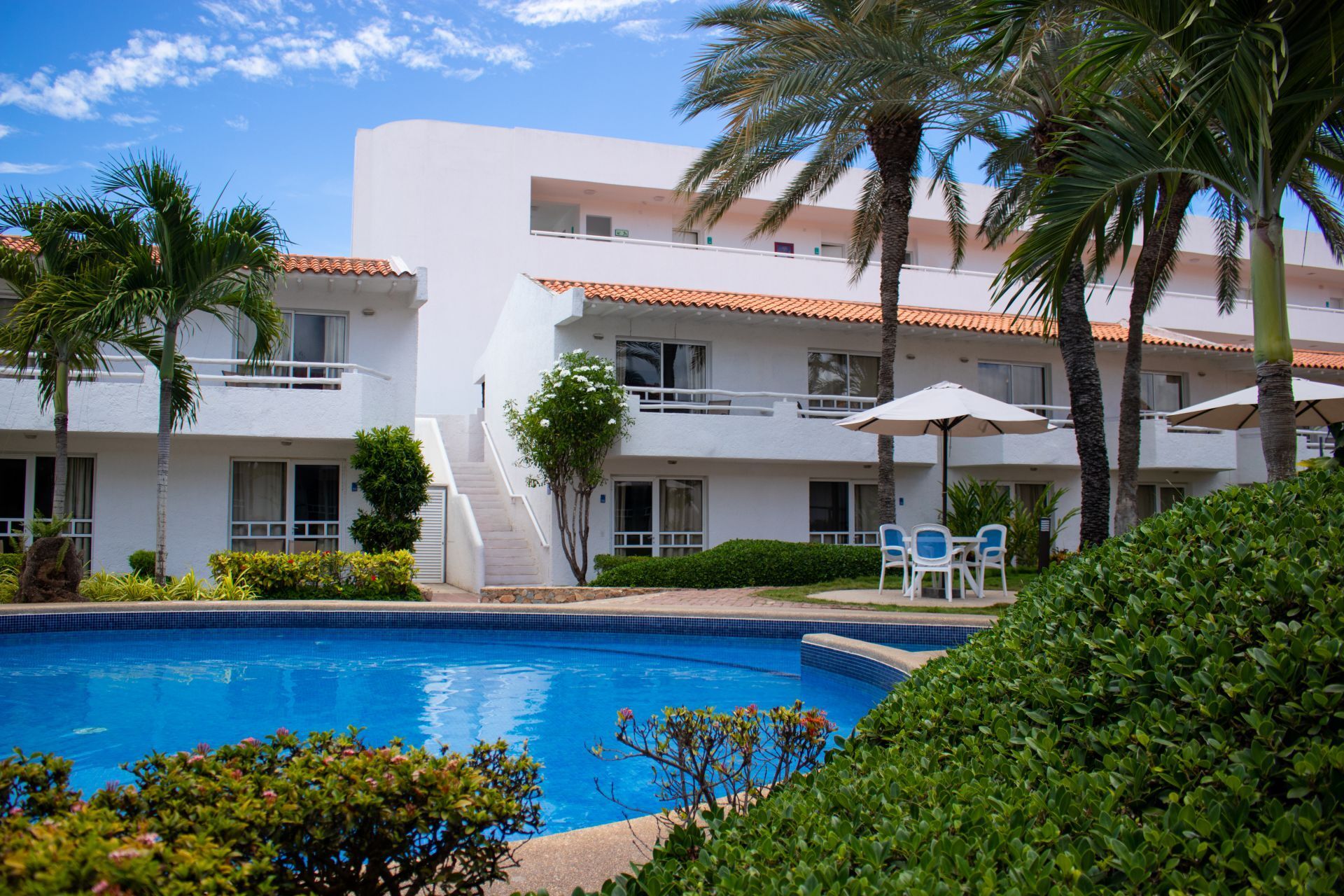 Piscina azul del LD Palm Beach en Playa el Agua, con tumbonas blancas y palmeras, bajo un cielo soleado y despejado.