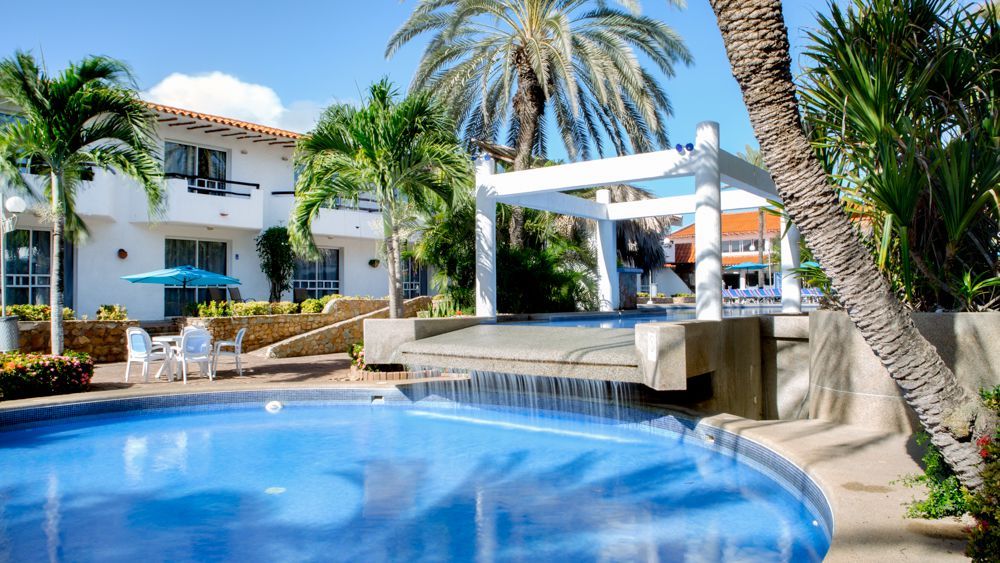 Piscina infantil con cascada en LD Palm Beach, Playa el Agua, rodeada de vegetación tropical.