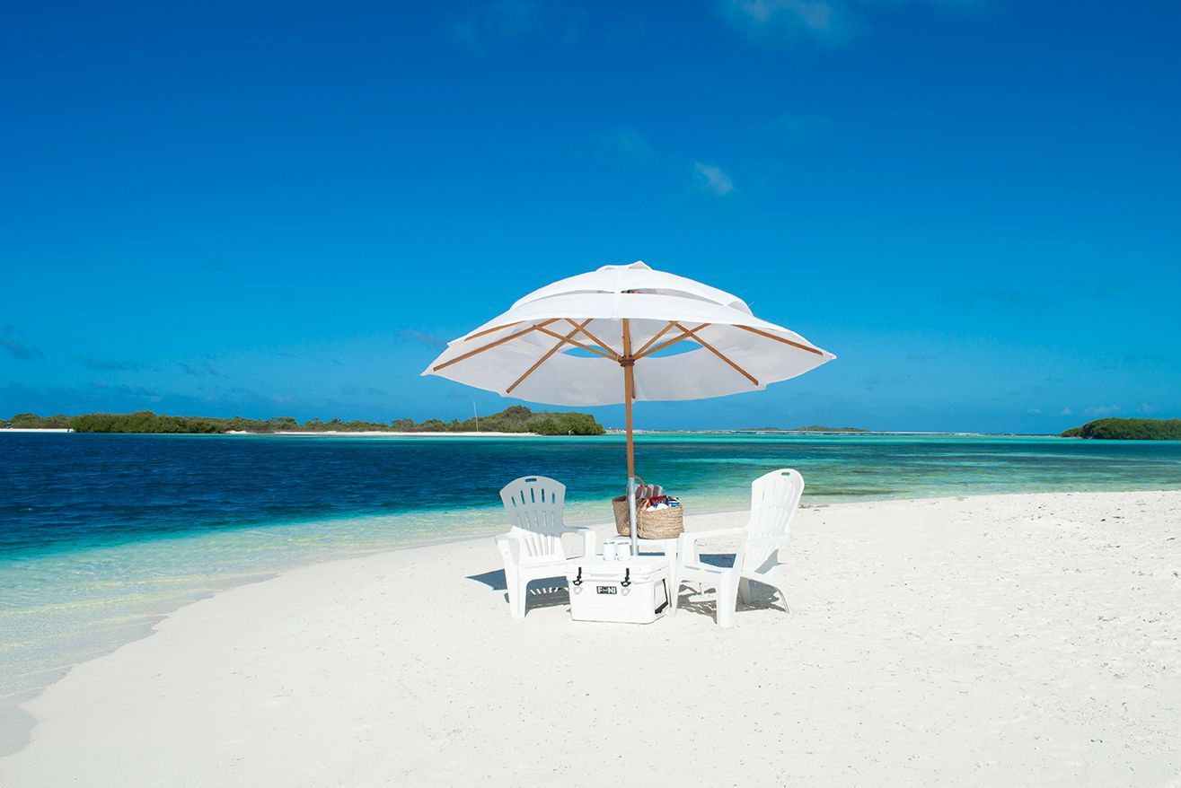Playa paradisíaca en Sabbia by LD, Los Roques, con sillas y sombrilla blanca frente al mar turquesa.