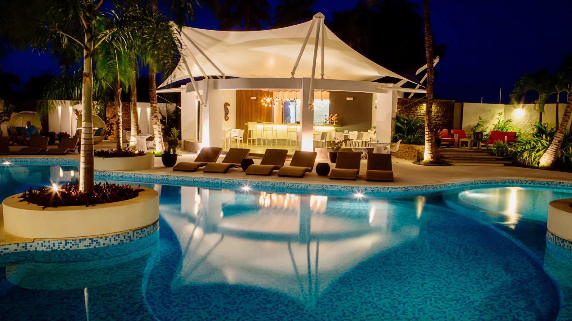 Piscina iluminada del H2Otel By LD, con tumbonas y cama balinesa, reflejando lujo y tranquilidad nocturna.
