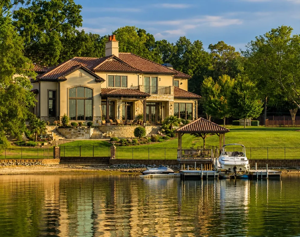 Lakefront villa with a dock and boat, framed by trees and reflected in calm water at sunset