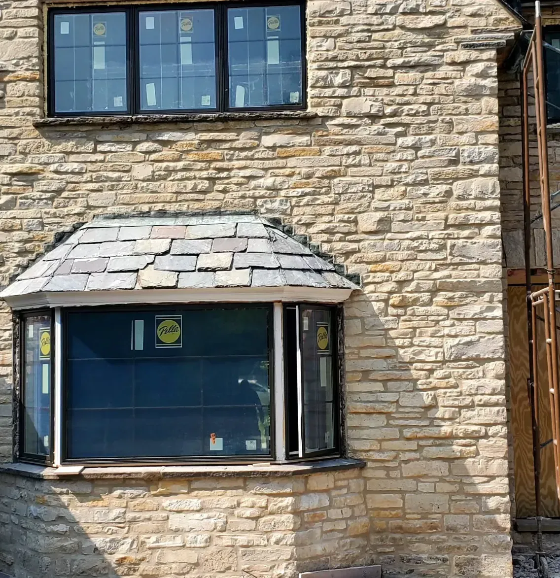 Stone building facade with blue-framed windows and a small bay window under a sloped shingle roof.
