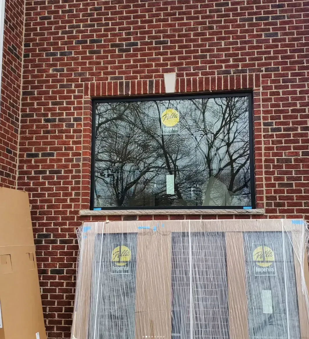 Brick wall with a window, tree reflections, and a plywood-covered section below during renovation.