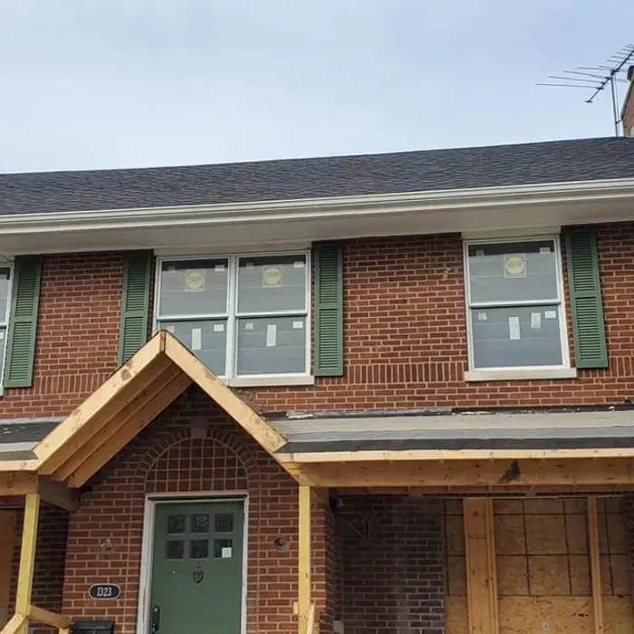Brick house exterior with green shutters, green front door, and an unfinished front porch and garage entrance