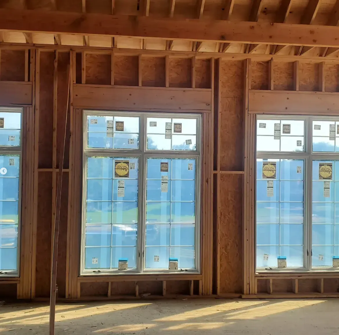 Interior framing of a room under construction with large windows and sunlight on the floor