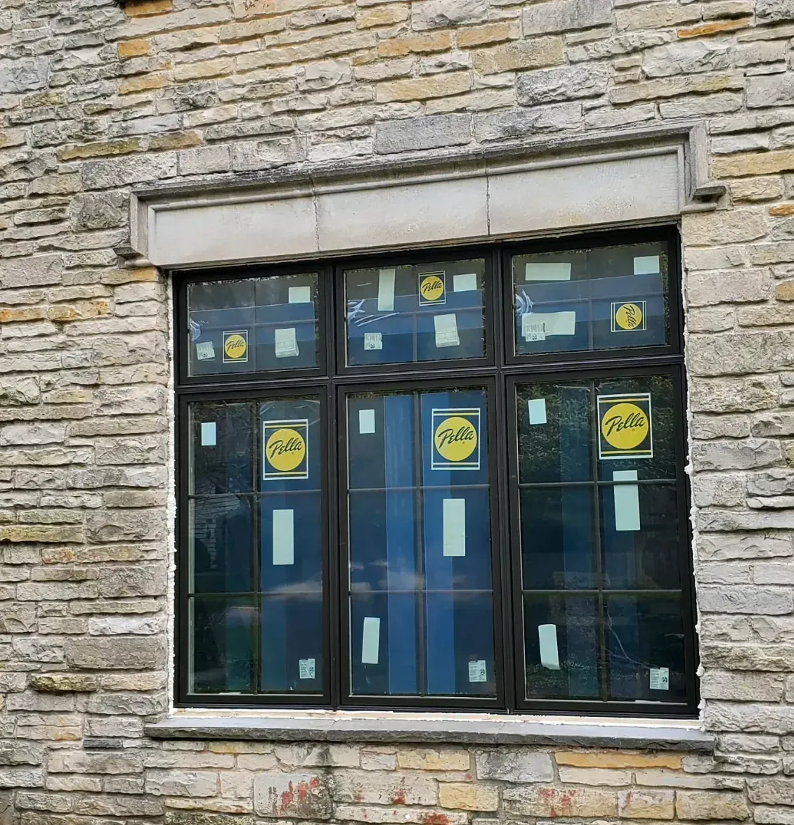 Stone building facade with a dark window covered in yellow stickers and paper notices