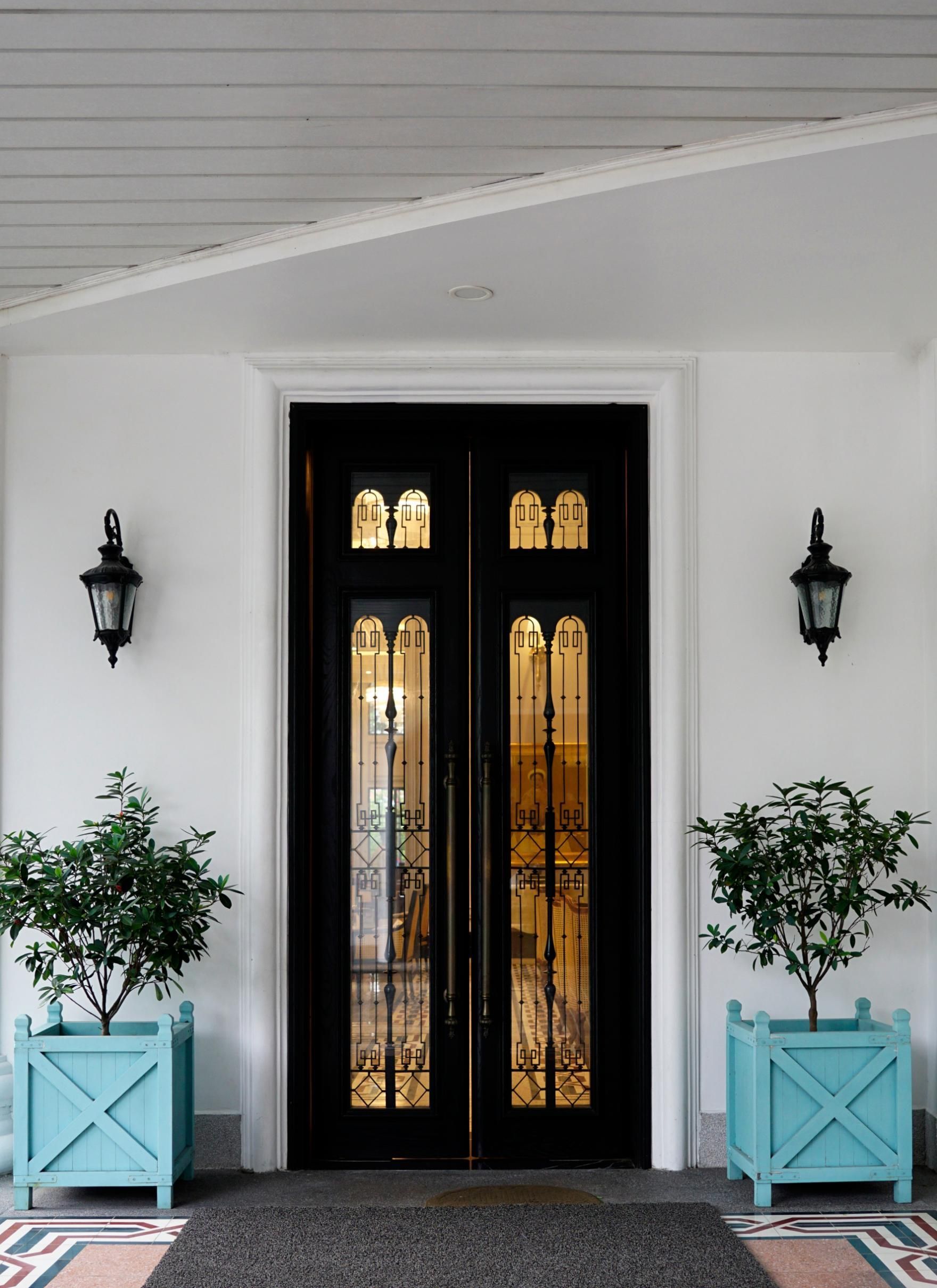 Black double front door with glass panels, flanked by wall lanterns and potted plants in turquoise planters