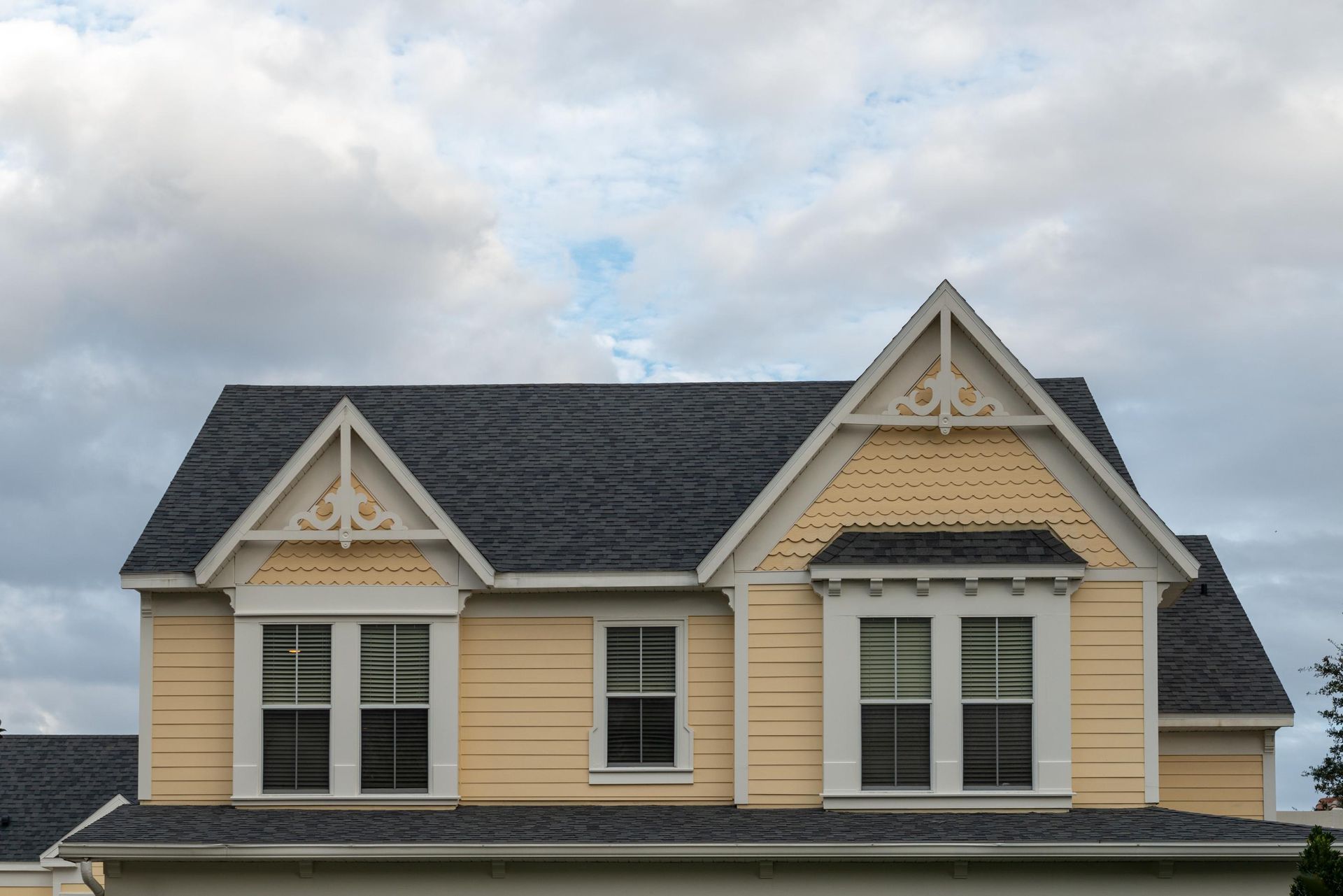 Yellow house roof with decorative gables under a cloudy sky
