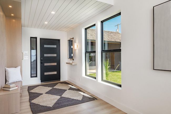 Modern entryway with black front door, windows, patterned rug, and white walls