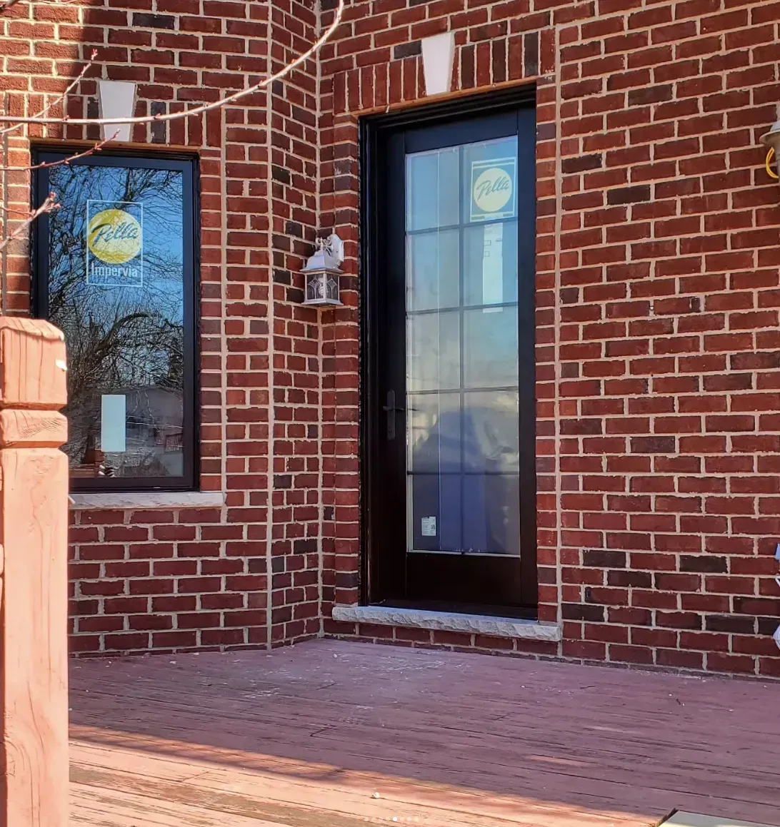Brick storefront entrance with a dark glass door and window beside a red brick wall.