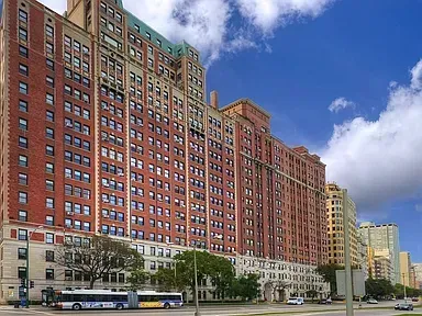 Tall red-brick apartment building along a city street under a blue, cloudy sky