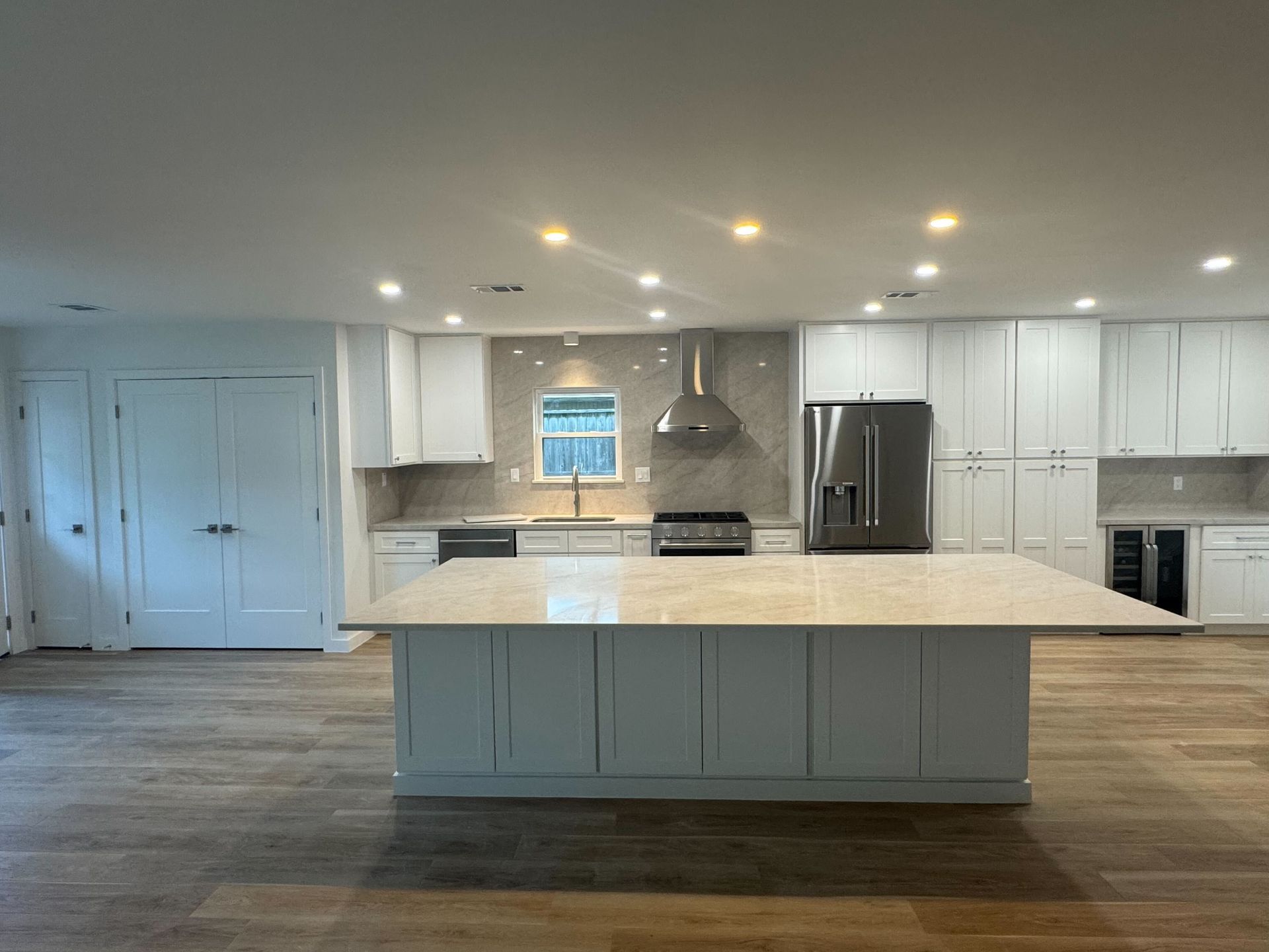 Modern white kitchen with large island, stainless appliances, and wood floors