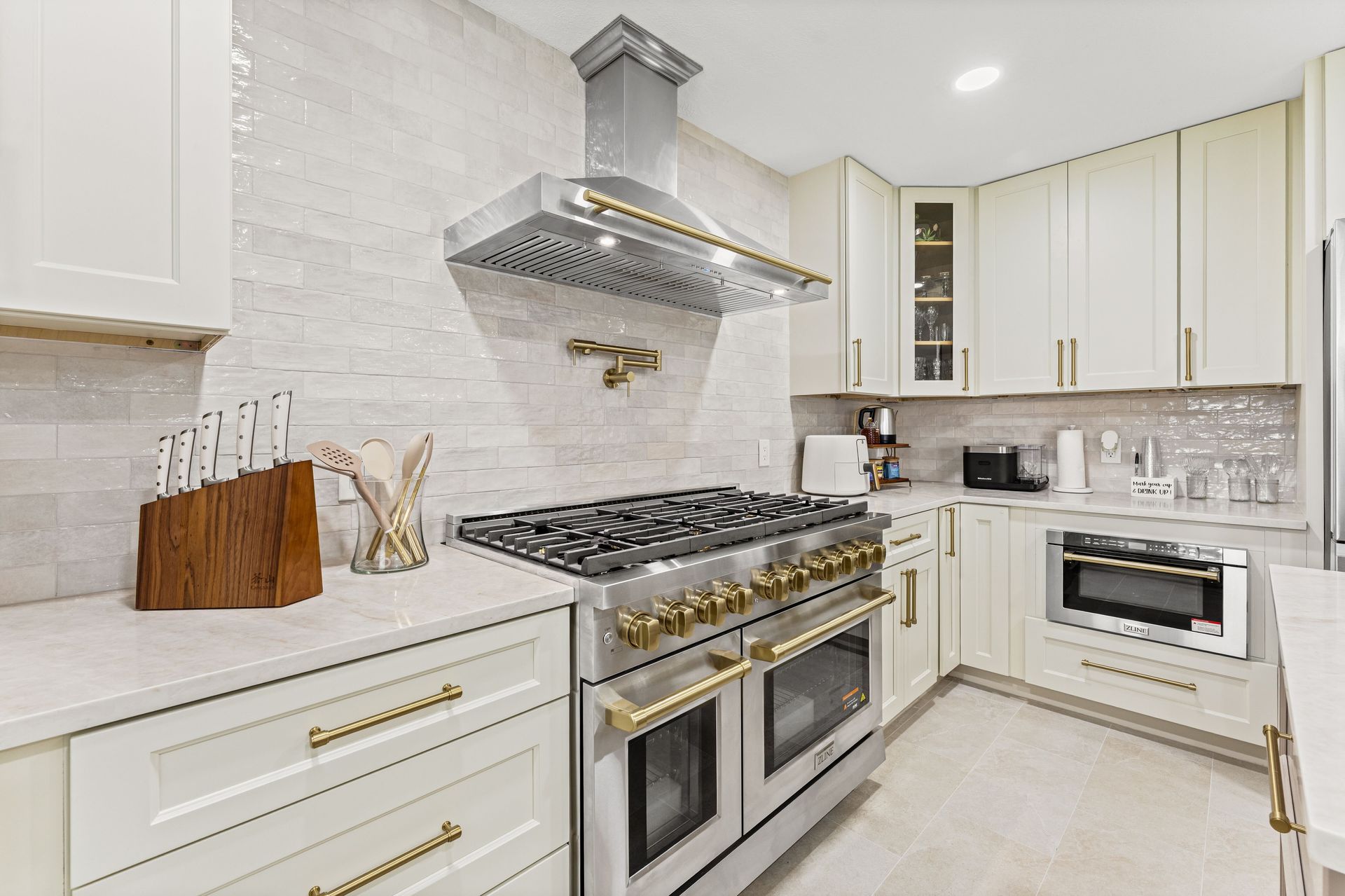 Bright modern kitchen with white cabinets, marble backsplash, and stainless steel stove with gold accents