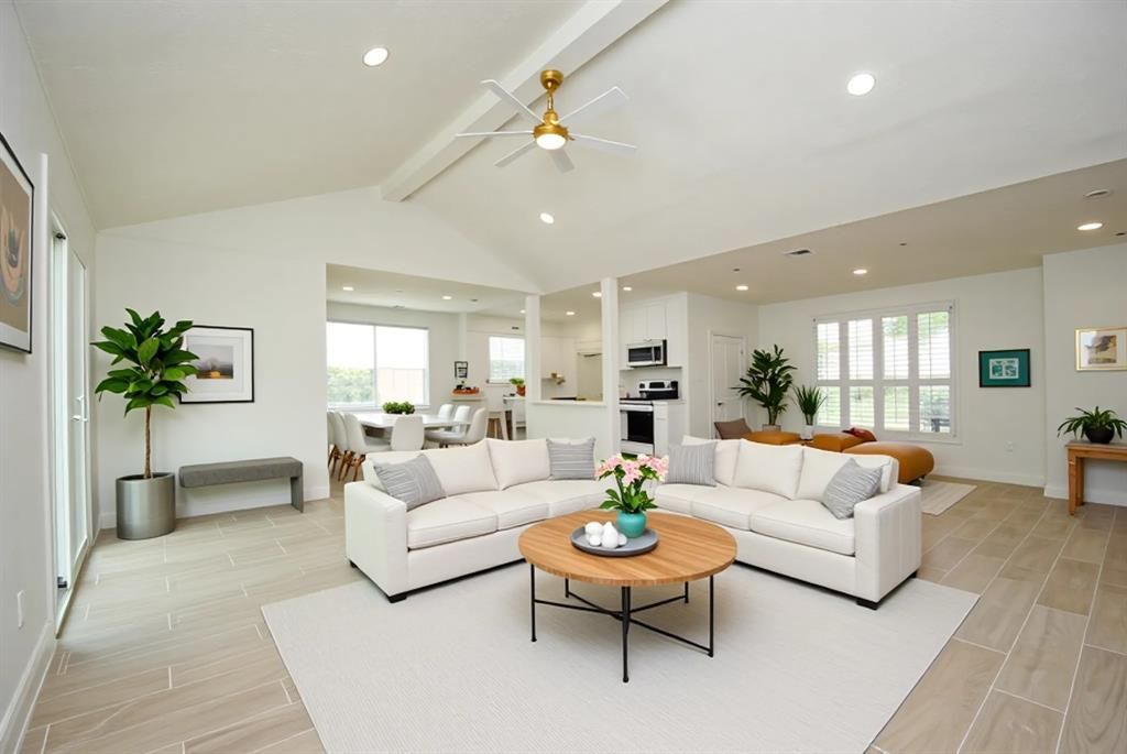 Spacious, bright living room with white sofas, a round coffee table, and plants.